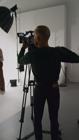 Vertical-Video-Of-Male-Film-Camera-Operator-Shooting-Movie-Or-Video-In-Studio-Using-Tripod